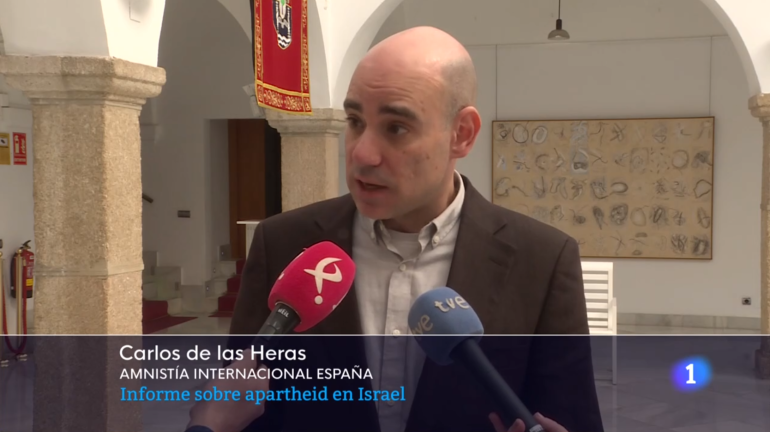 Carlos de las Heras hablando. En los rótulos puede leerse:Carlos de las Heras Amnistía Internacional España Informe sobre apartheid en Israel