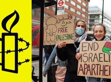 Una pareja sostiene dos pancartas de cartón. En una puede leerse FREE PALESTINE. En la otra se lee END ISRAELI APARTHEID.