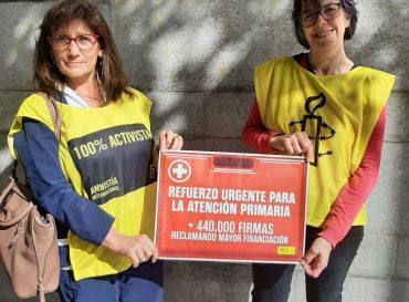 Dos activistas de Amnistía Internacional sosteniendo un cartel en el que se pide un refuerzo urgente para la atención primaria.