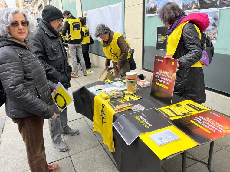Activistas de Amnistía Internacional, la mayoría con petos amarillos, junto a una mesa con folletos y otros materiales de la ONG.