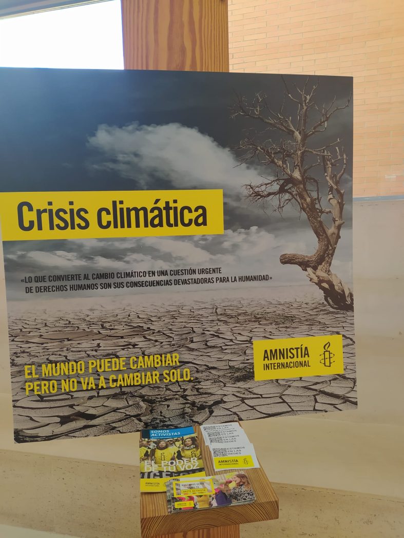 Cartel anunciador de la exposicón. Se ve un paisaje desértico con el título CRISIS CLIMÁTICA, el texto "Lo que convierte al cambio climático en una cuestión urgente de Derechos Humanos son sus consecuencias devastadoras para la Humanidad", el lema EL MUNDO PUEDE CAMBIAR, PERO NO VA A CAMBIAR SOLO, y el logo de Amnistía Internacional.
A los pies del cartel hay algunos folletos de Amnistía Internacional.