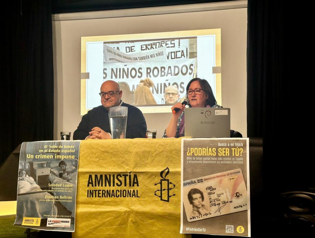 Esteban Beltrán y Soledad Luque tras una mesa. Al frente de la mesa cuelgan un cartel anunciando el acto, una lona de Amnistía Internacional y otro cartel con el lema ¿PODRÍAS SER TÚ?