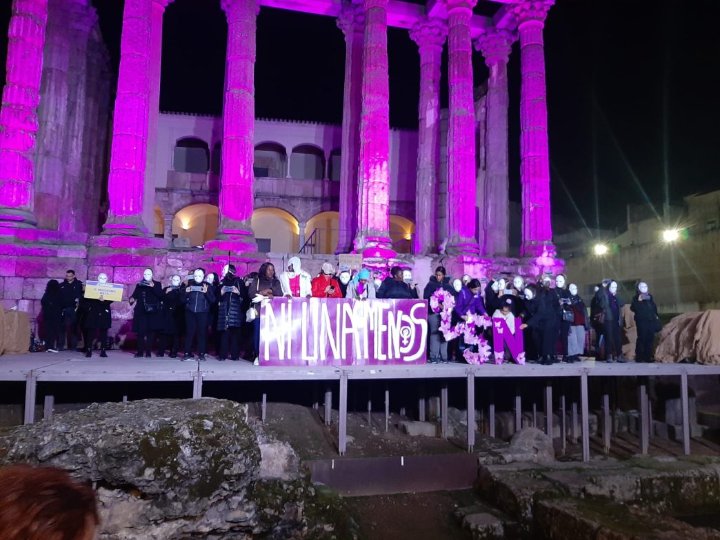 El Templo de Diana, en Mérida, iluminado con luces moradas. Un grupo de personas con máscaras blancas portan una pancarta con el lema NI UNA MENOS.