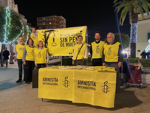 Militantes de Amnistía Internacional en Badajoz, con una pancarta con el lema POR UN MUNDO SIN PENA DE MUERTE. Ante ellos hay una mesa con materiales de Amnistía Internacional.