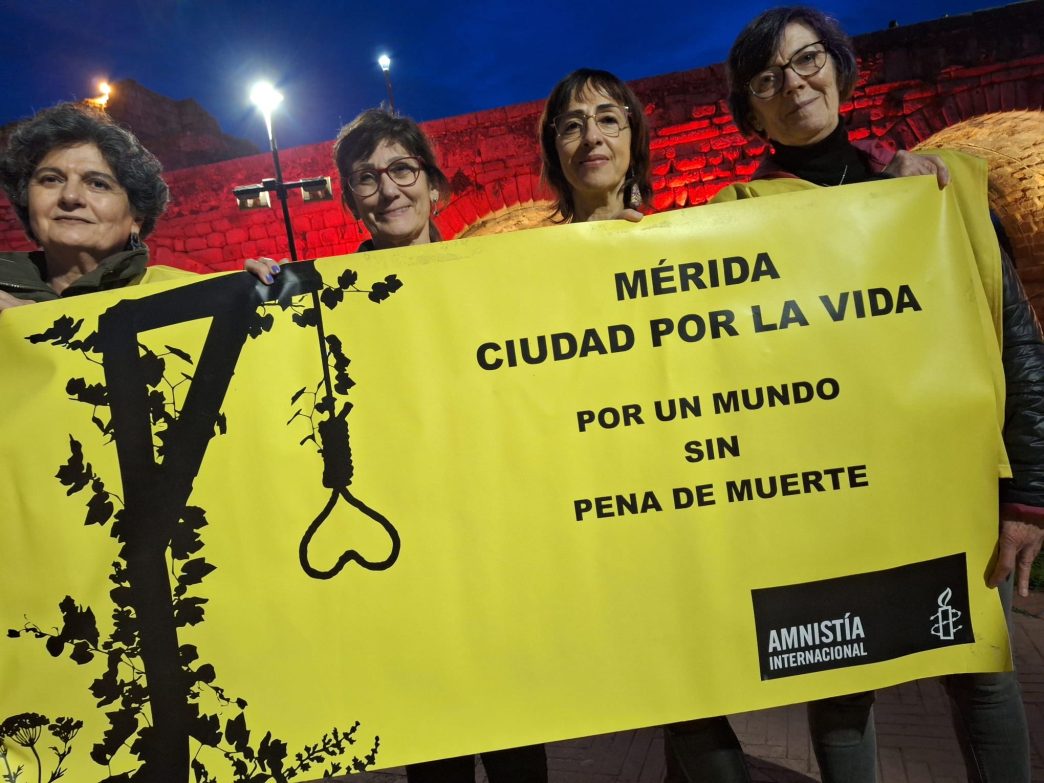 Cuatro compañeras de Amnistía Internacional, ante el Puente Romano de Mérida, sosteniendo una pancarta con el lema MÉRIDA CIUDAD POR LA VIDA, POR UN MUNDO SIN PENA DE MUERTE.