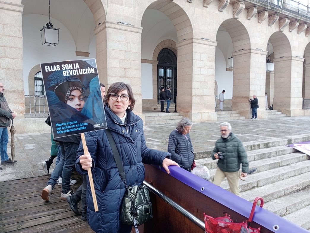 Nuestra compañera Marta, ante el Ayuntamiento de Cáceres, con una pancarta con el lema ELLAS SON LA REVOLUCIÓN sobre una fotografía de una mujer afgana.