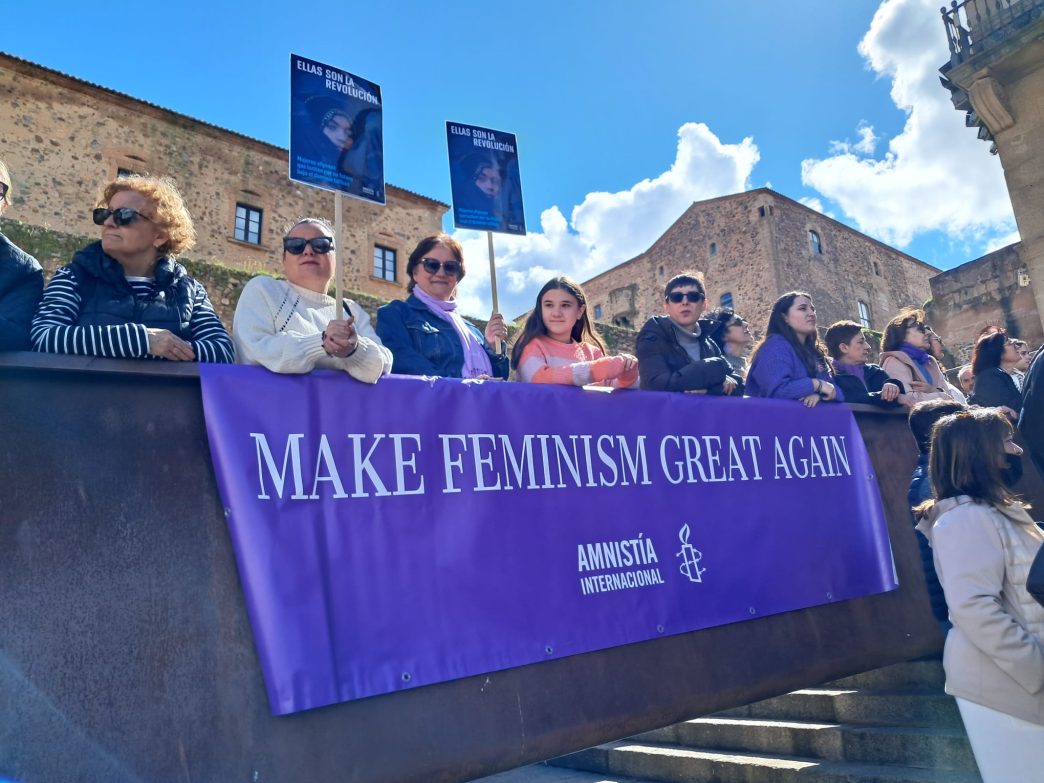 Activistas de AI Cáceres con una lona con el lema MAKE FEMINISM GREAT AGAIN.