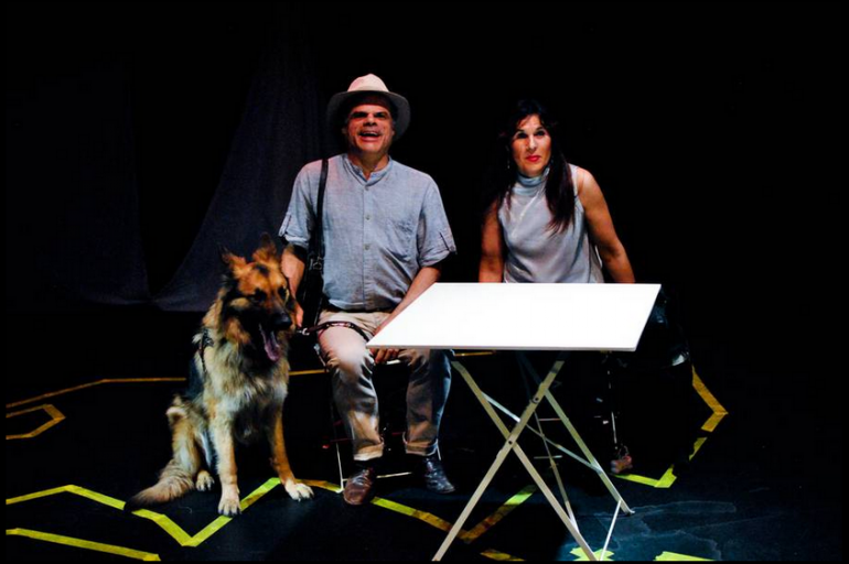 dos actores durante la obra sentados al lado de un perro