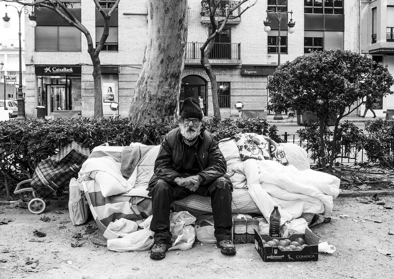 Un hombre indigente sentado en la calle en un sillón de bolsas llenas de enseres