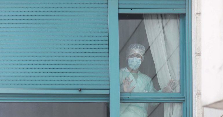 Una sanitaria con mascarilla mira desde una ventana de un centro sanitario con las manos apoyadas en el cristal de la ventana