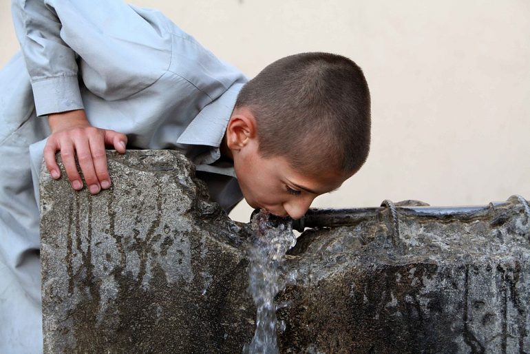 un niño bebe agua de un grifo común en el oeste de Kabul, Afganistán
