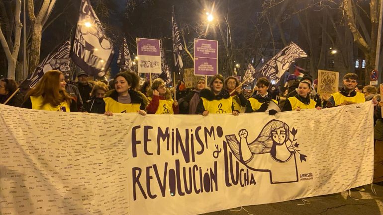 Pancarta Feminismo Revolución y Lucha sujeta por jóvenes activistas con peto de Amnistía Internacional en la manifestación del 8M