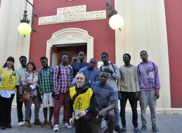 Fotografía de un grupo de jóvenes negros junto con dos miembros del equipo de AI Alcalá de Henares a la entrada del Teatro Salón Cervantes.